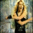 A woman with long blonde hair in a black sleeveless top holds a guitar, transitioning from crossed arms to extended arm pose against a blurred background.