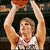A basketball player in a white jersey with red trim holds an orange ball above his head, captured across three showing slight movement