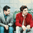 Static 48x48 pixel buddy icon showing two men in a blurred background, one in gray jacket with blue collar and black pants, the other in red jacket over white shirt with light pants, both facing right with neutral expressions.