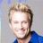 Pixelated image of a smiling person with light brown hair wearing a dark blue shirt against a gray background, with blue text blocks on a blue background.