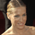Pixelated close-up of a person with light brown hair styled in an updo, wearing a strapless garment against a dark background.