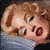 A 50x50 pixel animated contact sheet showing three sequential frames of a cartoon-style female character with blonde hair and red lipstick lying on her side, displaying subtle facial expression changes across the animation sequence.