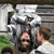 Pixelated static image of two people in a vehicle interior with visible greenery outside, likely from a movie scene.