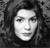 A grayscale pixelated portrait of a person with dark hair, closed eyes, and a neutral expression, set against a dark textured background.