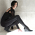 Pixelated figure in black attire crouches with one leg extended, hand resting on knee, against light gray background.