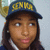 Pixelated image of a person wearing a dark blue cap with yellow text, long dark hair, and a white-collared shirt against a light gray background.