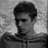 Black-and-white pixelated static image of a person's head and shoulders with short dark hair, visible facial features including eyes, nose, mouth, and ear, wearing a collared shirt or jacket against a light gray background.