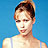 Pixelated portrait of a person with short dark hair tied up, wearing light-colored clothing against solid blue background.