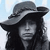 Pixelated grayscale image of a person wearing a wide-brimmed hat with long hair visible beneath, set against a light blue background.