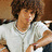 Pixelated image of a person with brown curly hair wearing a white shirt, holding a dark object near their face.