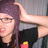 Pixelated image of a person with long dark hair wearing glasses and a black top, holding an object near their face.