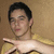 Pixelated image of a person with dark hair wearing a yellow garment with a white collar against a brown background.