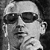 Black-and-white pixelated static icon of a person wearing dark sunglasses and a light-colored cap, with visible facial features including nose, mouth, and ear against a dark background.