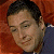 Pixelated close-up of a person with short dark hair, closed eyes, and a neutral expression against a reddish-brown background.
