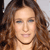 A pixelated close-up of a person with long brown hair, light skin, and a neutral expression, wearing a thin dark necklace.