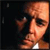 Pixelated close-up of a person's face with light skin tone, dark eyebrows, and dark eyes, set against a dark background with a white collar visible.