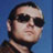 Static 48x48 pixel icon showing a person's face with dark hair and sunglasses against a blue background, rendered in low-resolution pixel art style.