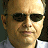 Pixelated close-up of a person with light skin tone wearing dark sunglasses and a light-colored collared shirt, cropped to show head and shoulders.