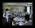 Two side-by-side pixelated frames show a classroom with students at desks, one frame with a red chair and visible wall text, the other with a different student arrangement.