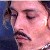 Pixelated close-up of a person's face with closed eyes, dark hair, and a mustache against a blue background.