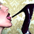 Pixelated close-up of a pink hand holding a black high-heeled shoe against a light beige background.