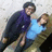 Two people in a close pose, one wearing dark clothing with purple accents and the other in light blue shirt, against textured background.