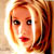 Pixelated static image of a woman's face with blonde hair and red lips, rendered in warm tones on a light background.