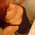A person with reddish-brown hair in a black sleeveless top, viewed from the side with a slight downward angle, showing a smiling expression.