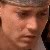 Pixelated close-up of a person's face with light skin tone, visible eyes, nose, mouth, and partial hair, set against a dark background.