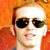 Pixelated close-up of a person with light skin wearing dark sunglasses, red hair tied back, and an orange background.