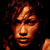 Pixelated static image of a person's face with warm brown and orange tones against black background, likely from early digital art or low-resolution capture.
