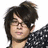 Pixelated image of a person with dark tousled hair and glasses, wearing a black-and-white patterned garment against white background.