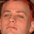 Pixelated close-up of a person's face with light skin tone, visible eyes, nose, mouth, and partial hair, rendered in warm brown and peach tones.