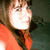 A person with brown hair and bangs wears a red sleeveless top, positioned against a dark background in four -aligned