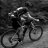 A grayscale pixelated image of a person riding a bicycle, viewed from the side with the figure slightly blurred.