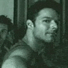 Two identical grayscale images of a man with short dark hair and light stubble, wearing a sleeveless shirt, positioned side-by-side against a blurred background.