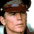 Pixelated static icon of a person with brown hair wearing a dark cap, visible facial features including eyes and mouth, light skin tone, and partial clothing details against a white background.