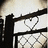 Pixelated image with brown background and white text reading "Locked In Your Heart Forever Nick <33" next to a chain-link fence structure.