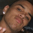 Pixelated close-up of a person's face with light brown skin tone, visible eye, nose, mouth, and ear showing white nail polish on the index finger.