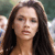 A pixelated close-up of a person with long dark hair, light skin, and neutral expression against a blurred background.