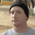 Pixelated static image of a person wearing a dark beanie and light-colored shirt, facing left with closed eyes against a blurred background.