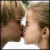 Two people in close proximity with lips touching, one wearing a white top against a blurred background.