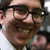 A smiling person with dark hair and glasses appears in a of four , each showing slightly different facial expressions