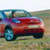 A red vehicle with blue accents is positioned on a grassy field under a light sky, viewed from a low angle.
