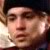 Pixelated close-up of a person's face with light skin tone, dark hair, and neutral expression against a dark background.