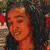 Pixelated close-up of a person with light brown skin tone, dark curly hair, and a black top against a blurred background with green and red elements.