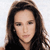 A static pixelated image of a person with long dark brown hair, light skin, and a neutral expression against a light background.