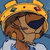 Animated cartoon character with brown fur, dark blue eyepatch, yellow crown-like headpiece with green and red gems, white shirt, and light blue background.