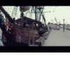 Animated sequence showing a person in red-and-white attire interacting with a large wooden ship on a dock, transitioning between close-up and wide shots.