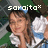 Pixelated image of a person with brown hair wearing white clothing, standing outdoors with green foliage in the background and text reading 'sakito' at top.